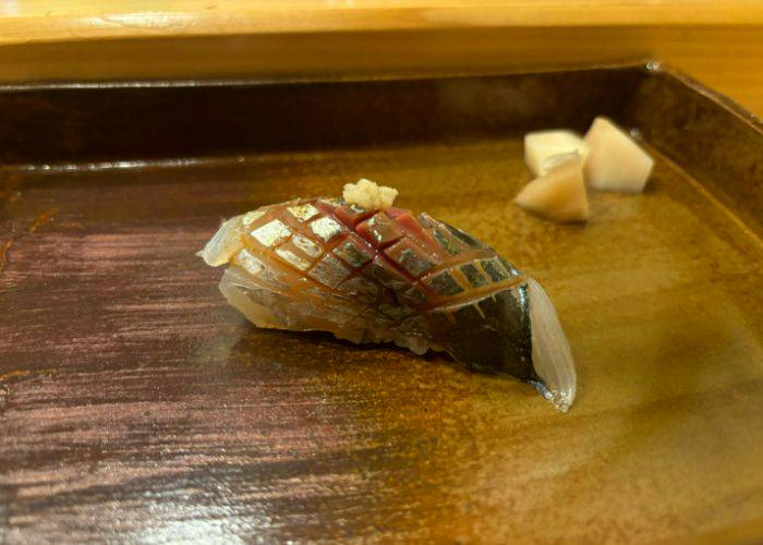 A cross-hatched nigiri sushi with soy sauce soaking into the cuts on the fish.